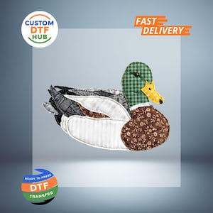 Peut inclure: Un canard en tissu avec une tête à carreaux verts, un bec jaune et un corps à motifs floraux marron. Le canard a des ailes et une queue à motifs gris, blancs et marron. L'image comprend le texte "CUSTOM DTF HUB", "FAST DELIVERY" et "READY TO PRESS DTF TRANSFER".