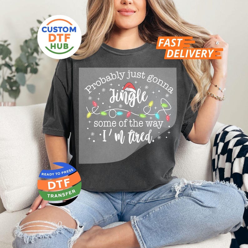 May include: Dark gray t-shirt with the text "Probably just gonna jingle some of the way, I'm tired." The design includes a Santa hat and Christmas lights. The shirt is a relaxed fit.