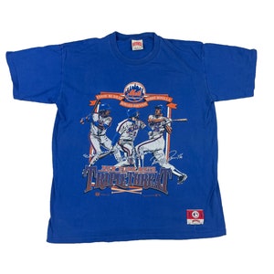 Puede incluir: Camiseta azul real con un gráfico de tres jugadores de béisbol en acción y el texto "New York Mets Triple Threat". La camiseta incluye los nombres de Eddie Murray, Howard Johnson y Bobby Bonilla.