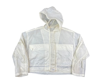 May include: A cropped off-white hooded jacket featuring long sleeves, a front button placket, and two chest pockets with button closures. The garment includes a small rectangular label at the bottom center with the text "HEARTS OF OAK".