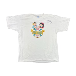 May include: White t-shirt with a Camp Cabbage 1998 10th Anniversary Cruise logo featuring two cartoon children in a boat. The logo is in yellow, green, blue, and red. The shirt has a signature on the top right corner.
