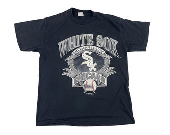 May include: Black t-shirt with a white graphic of the Chicago White Sox logo. The logo includes the team name, "White Sox", "American League", and "Chicago" in a stylized font. A baseball is featured in the center of the logo.