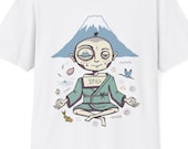 May include: A white short-sleeve t-shirt featuring a graphic of a figure in a teal robe sitting in a meditative pose. The figure has a box on their chest labeled STILL and a mountain in the background with small icons of a fish, bird, and petals.