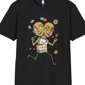 May include: A black short-sleeve t-shirt featuring a graphic of a two-headed character with a box-shaped torso labeled TWO FACED. The illustration includes speech bubbles, a smartphone, and small icons surrounding the character on the chest.