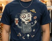 May include: Navy blue t-shirt featuring a cartoon character with a coffee cup, donut, and other graphics. The character wears a hoodie with the text "Never Sleep". The shirt is worn by a person.