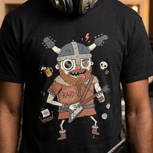 May include: Black t-shirt featuring a cartoon Viking playing an electric guitar. The Viking has a helmet with guitar-shaped horns, a beard, and the word "RAID" on the shirt. Additional graphics include a skull, beer mug, and lightning bolts.