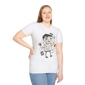 Op de afbeelding: Wit t-shirt met een cartoonfiguur met een doosvormige torso en de tekst "Quiet Rush". Het personage draagt een chirurgisch masker en houdt verschillende voorwerpen vast. Het t-shirt wordt door een persoon gedragen.