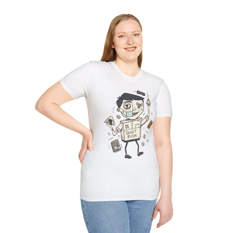 Op de afbeelding: Wit t-shirt met een cartoonfiguur met een doosvormige torso en de tekst "Quiet Rush". Het personage draagt een chirurgisch masker en houdt verschillende voorwerpen vast. Het t-shirt wordt door een persoon gedragen.