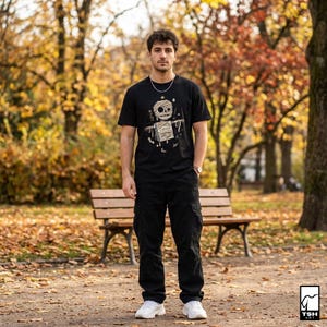 Puede incluir: Camiseta negra con un gr&aacute;fico de momia y la palabra "Cursed". La persona lleva pantalones cargo negros y zapatillas blancas. El fondo es un parque con un banco y follaje oto&ntilde;al.