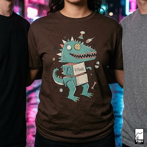 May include: Brown t-shirt featuring a cartoon dinosaur with a blue body, holding a box with the word "RAWR". The dinosaur has a large eye and is decorated with a party hat and a shooting star. A bone and an egg are also included in the design.