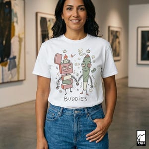 May include: White t-shirt with a cartoon graphic of a lighter and a marijuana joint holding hands, with the word "BUDDIES" below. The lighter has a pink top and the joint is green. The woman is wearing blue jeans.