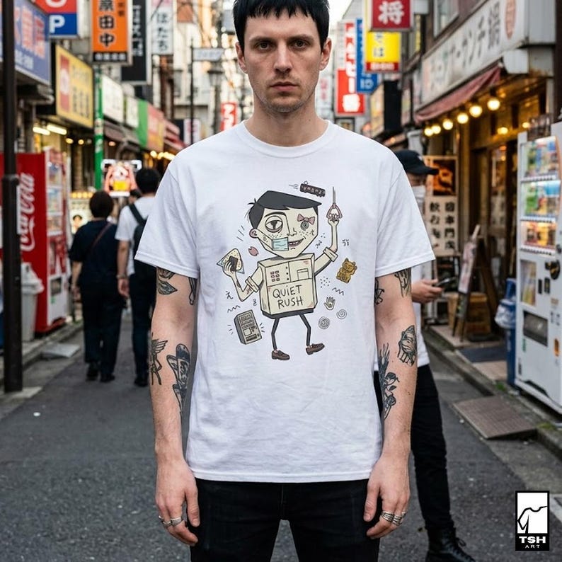 Op de afbeelding: Wit t-shirt met een cartoon illustratie van een persoon in een doos, met een gezichtsmasker en een kaartje en een schaar. De tekst "QUIET RUSH" staat op de doos. De persoon staat op straat.
