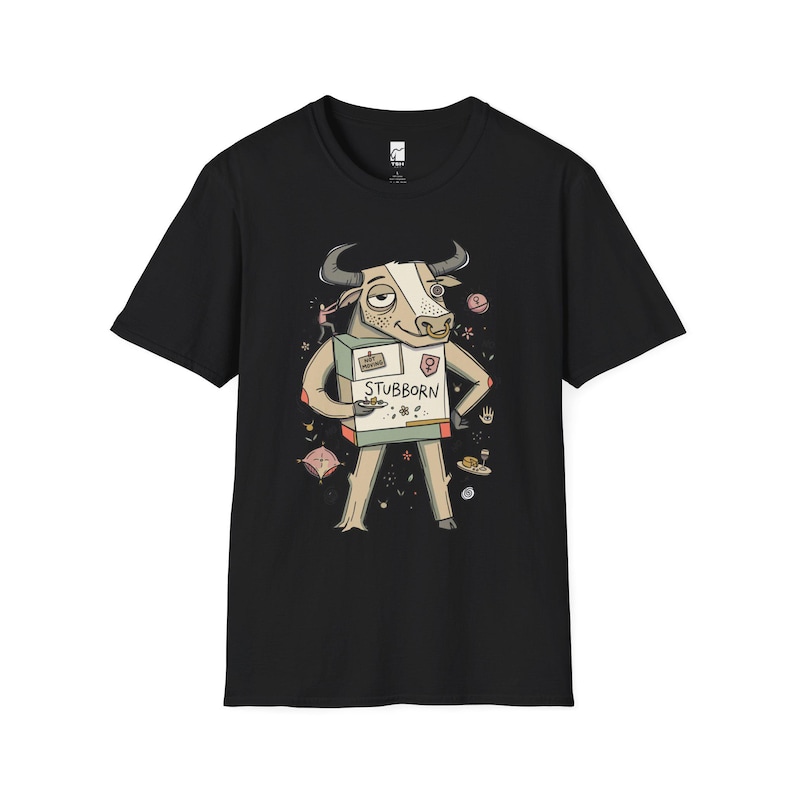 May include: A black short-sleeve t-shirt featuring a graphic illustration of a bull with a nose ring, wearing a box labeled STUBBORN. The bull is surrounded by small decorative icons including flowers, a hand, and a plate of food on a dark background.