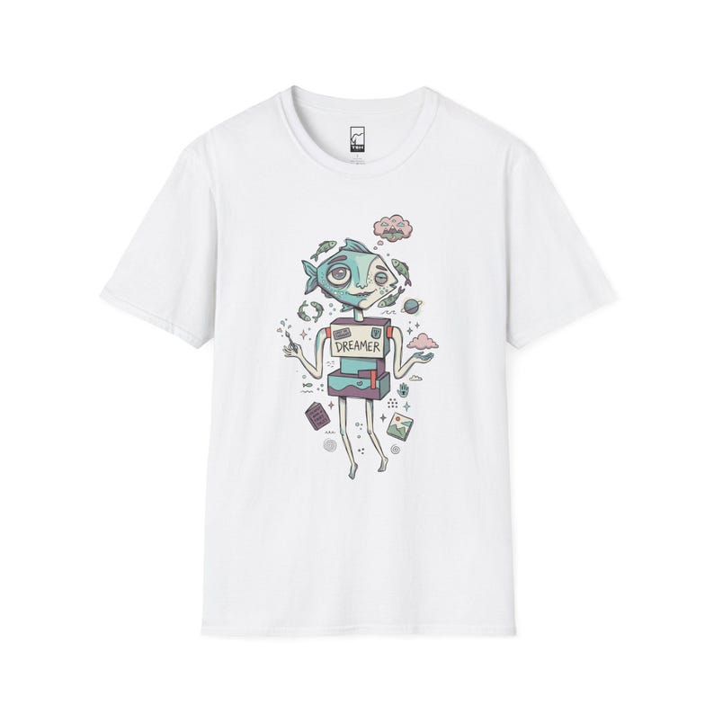May include: A white short-sleeve t-shirt featuring a graphic illustration of a fish-headed robot character with the word DREAMER printed on its chest. The design includes small floating elements like fish, clouds, a planet, and books in muted colors.