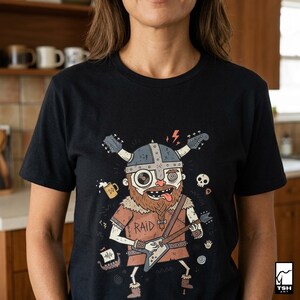 May include: Black t-shirt featuring a cartoon Viking playing a guitar. The Viking has a beard, helmet, and the word "RAID" on the shirt. Other graphics include a skull, lightning bolt, and a mug of beer.