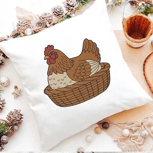 May include: White square pillow featuring a brown hen sitting in a woven basket. The hen has a red comb and wattle. The pillow is decorated with a farm animal theme.