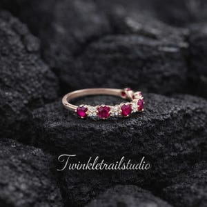 May include: A rose gold ring featuring alternating red gemstones and small clear stones. The ring is set against a dark, textured background. The text "Twinkletrailstudio" is visible in the lower portion of the image.