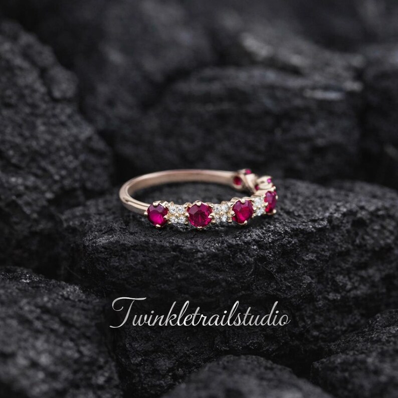 May include: A rose gold ring featuring alternating red gemstones and small clear stones. The ring is set against a dark, textured background. The text "Twinkletrailstudio" is visible in the lower portion of the image.