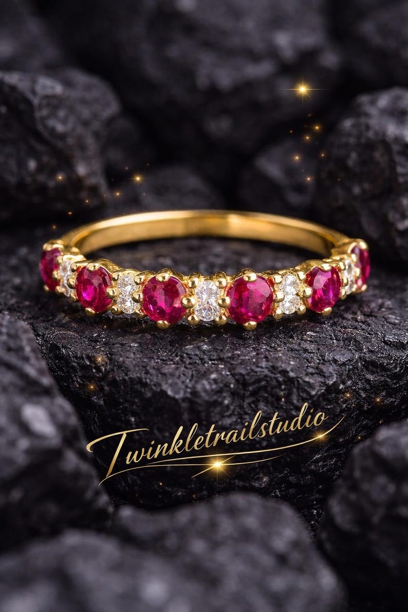 May include: A gold band ring with alternating red gemstones and small white gemstones. The ring is set against a dark, textured background. The text "Twinkletrailstudio" is in gold script.