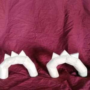 Peut inclure: Quatre sculptures de dragons en bois dans différentes poses. Les sculptures sont peintes dans une couleur claire et neutre et présentent une série de pointes triangulaires le long de leur dos. Les sculptures de dragons sont disposées sur un fond en tissu bordeaux.