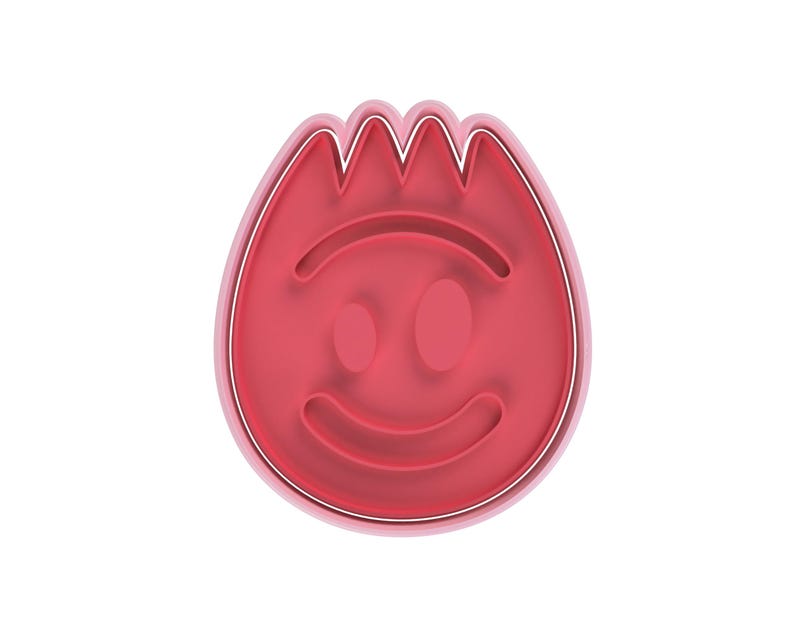 May include: A red plastic cookie cutter in the shape of a smiling face with a flame-like top. The cutter has a smooth, rounded shape with a thin white outline.