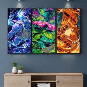 May include: A triptych of framed art prints featuring vibrant illustrations of Pokémon characters. The artwork showcases a blue Blastoise, a green Venusaur, and an orange Charizard, each set against dynamic backgrounds. The prints are displayed above a wooden media console.