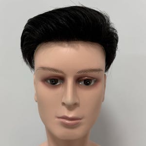 Könnte beinhalten: Ein Schaufensterpuppenkopf mit einer kurzen, schwarzen, gestuften Frisur. Die Schaufensterpuppe hat gemalte Augenbrauen, Augen und Lippen. Der Hautton ist ein helles Pfirsich. Der Hintergrund ist einfarbig weiß.