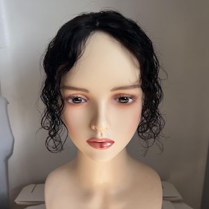 May include: A mannequin head with a realistic face and dark, wavy hair. The hair is styled with loose curls around the face. The mannequin has brown eyes and a neutral expression, showcasing a wig or hairpiece.