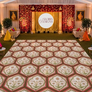May include: An event space with a patterned floor, white sofas, and a stage. The floor features a repeating floral design in shades of brown, red, and cream. The stage has a gold backdrop with the text "GLORIA DESIGNS".