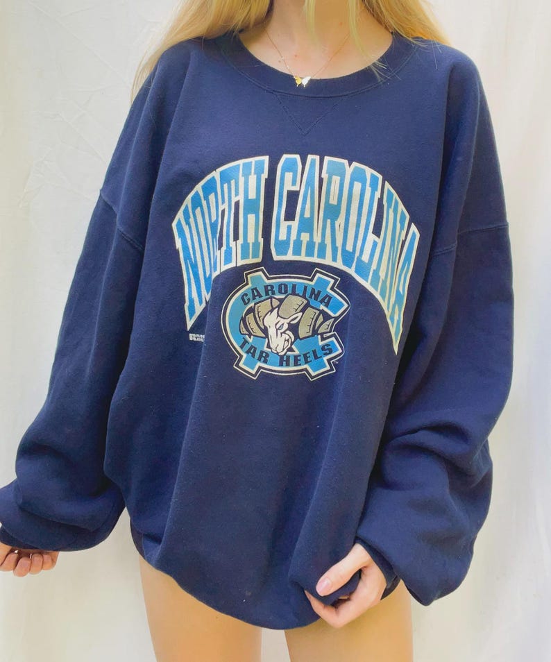 May include: Navy blue sweatshirt with the words "North Carolina" in light blue arched across the top. Below the text is a logo with a ram and the words "Tar Heels". The sweatshirt has long sleeves and a crew neck.