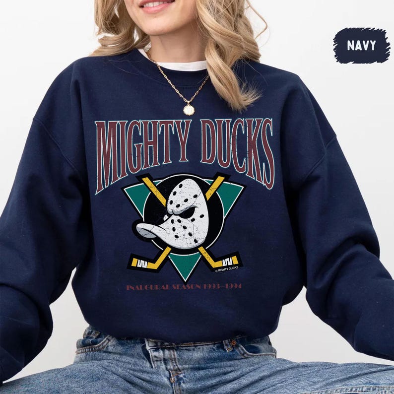 May include: Navy blue sweatshirt featuring the text "MIGHTY DUCKS" in maroon and a hockey mask graphic. Below the graphic is the text "INAUGURAL SEASON 1993-1994". The sweatshirt has a crew neck and long sleeves.