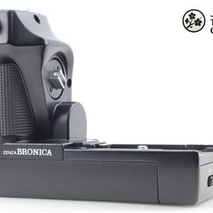 Puede incluir: Una taza de cerámica blanca con asa negra y el texto "But First, Coffee" en negrita negra. La taza se encuentra sobre un fondo borroso, sugiriendo un ambiente acogedor.