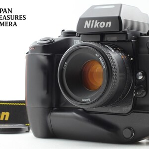 Może przedstawiać: Czarny aparat analogowy Nikon F4 z zamocowanym obiektywem Nikon AF Nikkor 50mm f/1.8. Aparat posiada wyraźny wizjer pentapryzmatyczny, czarny uchwyt oraz czarny pasek z nadrukowanym żółtym logo Nikon na materiale.