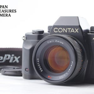 Könnte beinhalten: Eine schwarze Contax Aria 35mm Filmkamera mit einem Carl Zeiss Planar 1.4/50 Objektiv und der sichtbaren Seriennummer 5940140. Das Kameragehäuse hat einen Riemen mit der Aufschrift FinePix und der Text Japan Treasures Camera steht oben links.