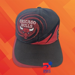 Könnte beinhalten: Eine schwarze Baseballkappe mit dem Chicago Bulls Logo, das in Rot und Weiß auf die Vorderseite gestickt ist. Das Design umfasst ein rotes, kreisförmiges Grafikmuster, einen schwarzen Schirm und rote Akzente an den Seitenteilen der Krone.
