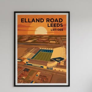 Puede incluir: Póster enmarcado del estadio Elland Road en Leeds, Inglaterra, con un fondo de puesta de sol. La obra de arte presenta una ilustración detallada del estadio, con el texto "ELLAND ROAD LEEDS" en la parte superior. El póster está sobre un sofá gris.