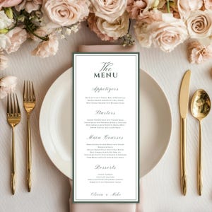 May include: A wedding menu card with a green border and elegant script. The menu is placed on a white plate with gold silverware. Soft pink and cream-colored roses are arranged around the plate, creating a romantic setting.