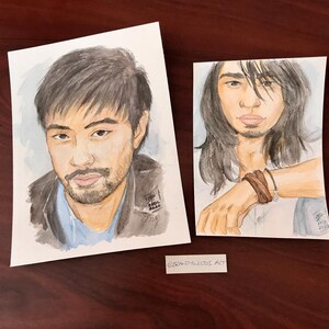 May include: Two watercolor paintings of people. The first painting is of a person with dark hair and a beard, wearing a dark jacket and a light blue shirt. The second painting is of a person with long dark hair, wearing a white shirt and a brown bracelet. Both paintings have a light blue background.