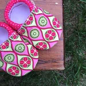 May include: A pair of pink baby booties with a green and pink floral pattern. The booties are made of fabric and have a soft, comfortable lining.