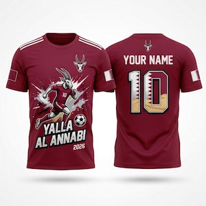 Puede incluir: Camiseta de f&uacute;tbol granate con rayas blancas en los hombros. La parte delantera presenta una gacela de dibujos animados con uniforme de f&uacute;tbol, el texto "Yalla Al Annabi 2026" y un bal&oacute;n de f&uacute;tbol. La parte trasera tiene el n&uacute;mero 10 y espacio para un nombre.