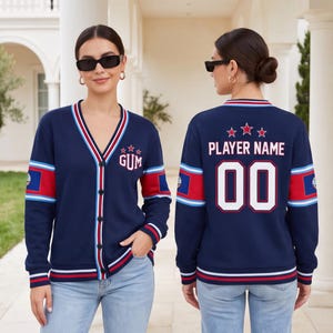 May include: A navy blue V-neck cardigan with button fastenings, featuring red and white striped trim. The front displays the text GUM with three stars, while the back shows the text PLAYER NAME and the number 00 with three stars above it.
