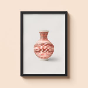 Könnte beinhalten: Gerahmter Druck einer Keramikvase mit rotem Polka-Dot-Muster. Die Vase hat einen weißen Sockel und Rand. Das Kunstwerk wird vor einem weißen Hintergrund in einem schwarzen Rahmen präsentiert, der an einer hellpfirsichfarbenen Wand befestigt ist.
