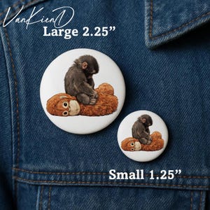 May include: Two white buttons with an illustration of a baby monkey sitting on a teddy bear. The large button is 2.25 inches, and the small button is 1.25 inches. The buttons are on a denim jacket.