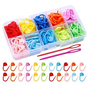 May include: A clear plastic organizer filled with colorful knitting stitch markers in red, orange, pink, yellow, green, and blue. Two long, thin yarn needles in red and purple are also included. Additional stitch markers are displayed below.