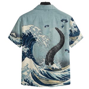 May include: Short-sleeved button-up shirt with a light blue background and a Japanese-inspired wave design. The design includes a large wave, a dark creature, boats, and flying saucers. The shirt has a classic collar and a relaxed fit.