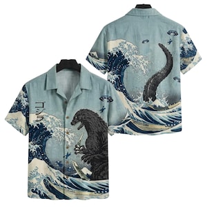 May include: Light blue short-sleeve button-down shirt featuring a Godzilla graphic in the style of The Great Wave off Kanagawa. The shirt has a classic collar and a relaxed fit, with a Japanese text on the front.
