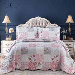 May include: A patchwork quilt set with a floral design in pink, grey, and white. The set includes a quilt and two pillow shams. The bed is styled with a cream-coloured headboard and matching bedside tables with lamps.