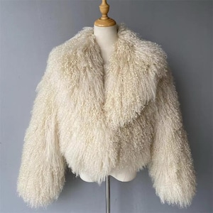 May include: Cream-coloured, fluffy jacket with a wide collar and long sleeves. The jacket is made of a soft, textured material, and is displayed on a mannequin. The jacket is a stylish outerwear piece.