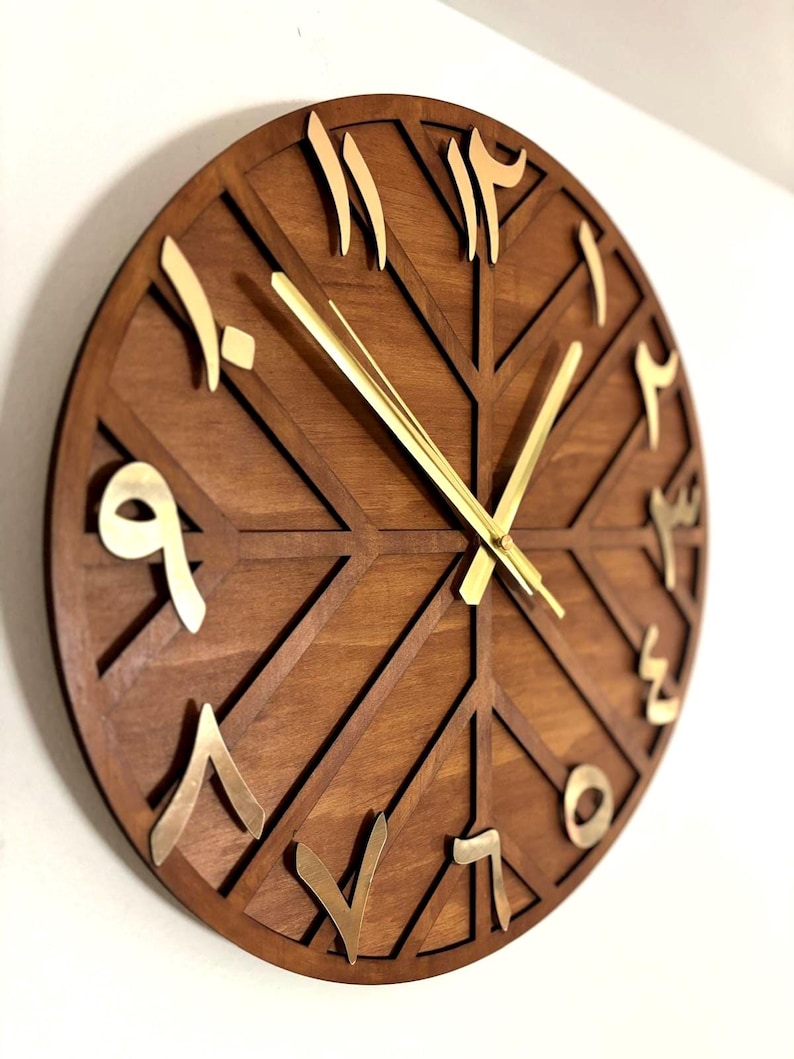 K&ouml;nnte beinhalten: Eine runde Wanduhr aus Holz mit geometrischem Design. Das Zifferblatt ist braun mit goldfarbenen arabischen Ziffern und Zeigern. Das Design der Uhr weist eine Reihe sich kreuzender Linien auf, die ein einzigartiges Muster bilden.