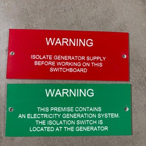 May include: Two rectangular warning signs. The top sign is red with white text that reads "WARNING" and "ISOLATE GENERATOR SUPPLY BEFORE WORKING ON THIS SWITCHBOARD." The bottom sign is green with white text that reads "WARNING" and "THIS PREMISE CONTAINS AN ELECTRICITY GENERATION SYSTEM. THE ISOLATION SWITCH IS LOCATED AT THE GENERATOR."